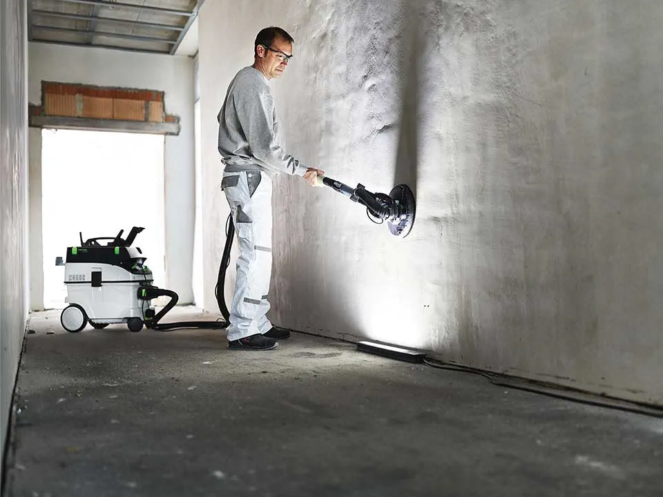 Käsityöläinen valaisee seinän valon avulla ja hioo sen alas